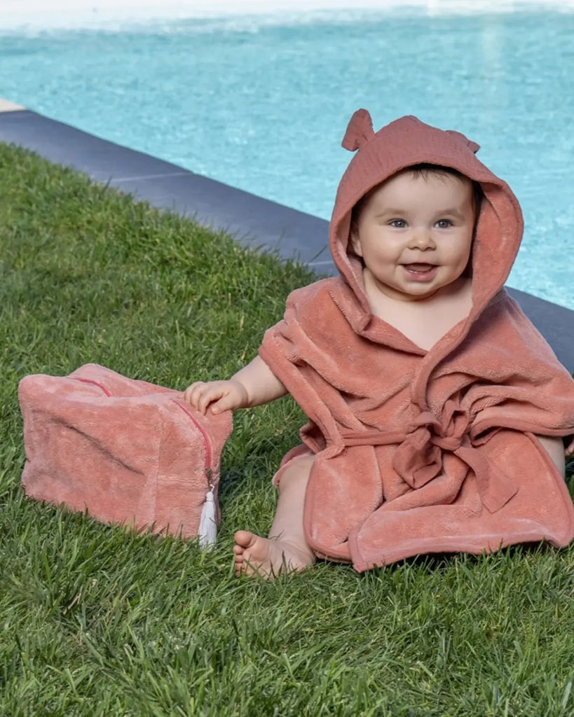 Photo d'un bébé dans sa serviette de bain à capuche marsala avec sa trousse de toilette marsala également