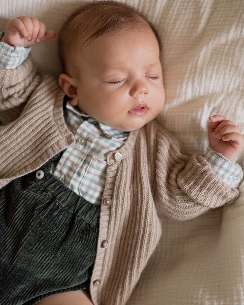 Bébé qui dort portant un bloomer vert sapin en velours associé à une chemise à carreaux et un gilet crème noisette