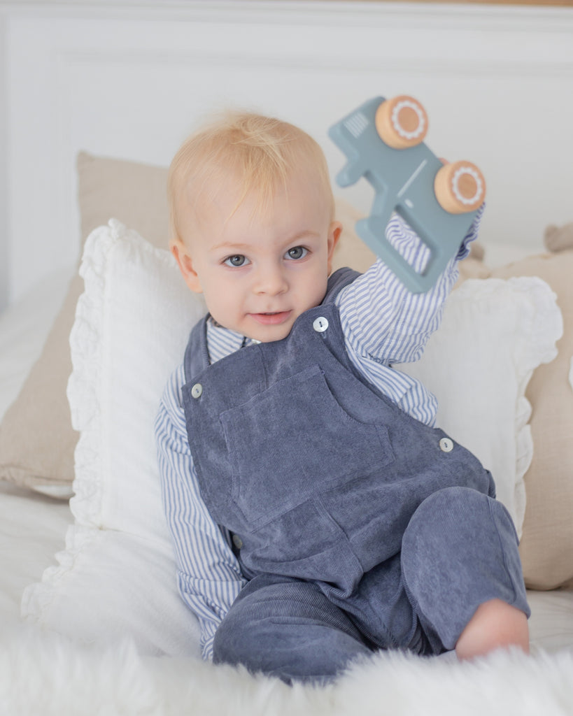 Bébé vêtu d'une chemise à rayures blanches et bleues et d'une salopette en velours bleue.