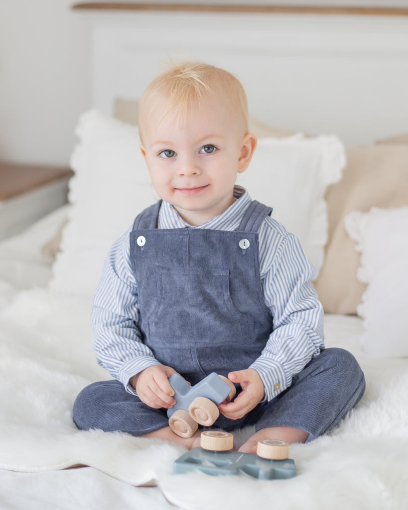 Bébé vêtu d'une chemise à rayures blanches et bleues et d'une salopette en velours bleue.