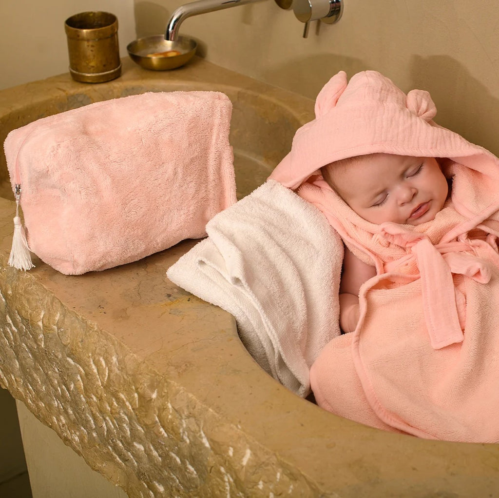 Photo d'un bébé dans sa serviette de bain à capuche rose et sa trousse rose blush à côté de lui