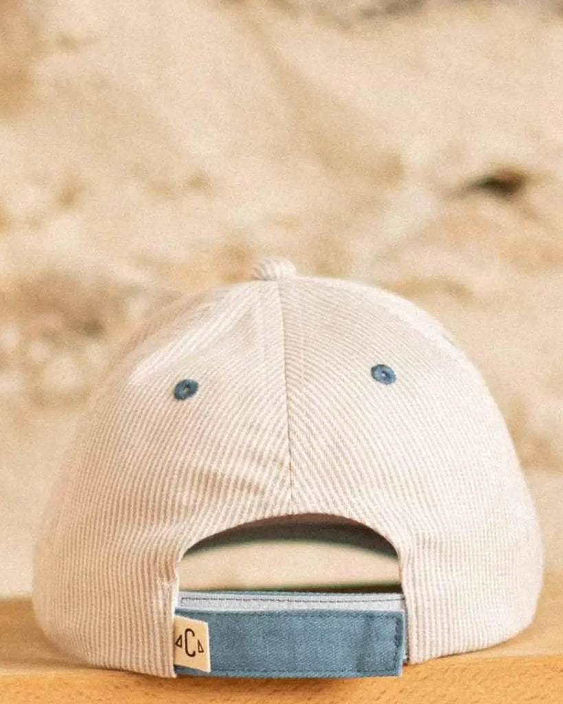 Vue de l'arrière de la casquette pour bébé à rayures beige et à broderie "Petit amour" bleue de la marque Bobine Paris.