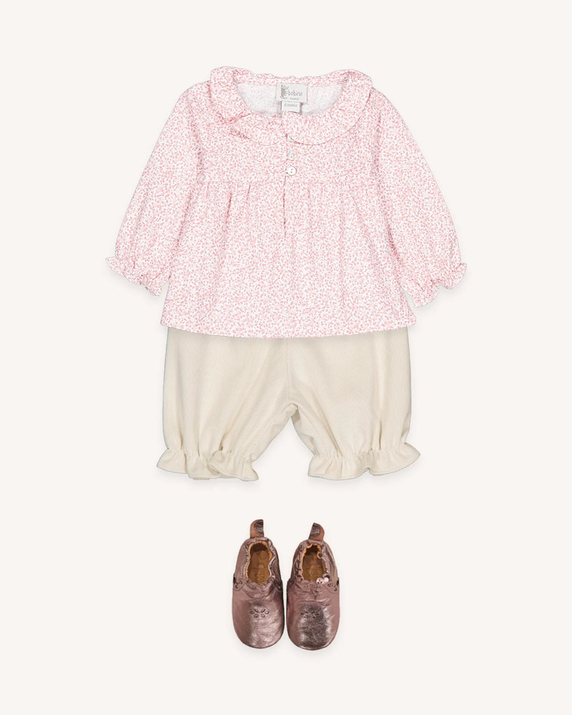 Look pour bébé fille composé d'une blouse fleurie rose et d'un bloomer en velours écru avec des petits chaussons rose métalliques de la marque Bobine Paris.